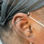 ndustrial piercing at Titan Piercing. The image showcases an industrial piercing, with a barbell connecting two holes in the upper ear cartilage, demonstrating the studio's expertise in complex and striking ear piercings.